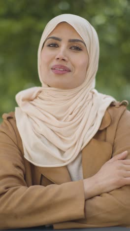 Vertical-Video-Portrait-Of-Smiling-Muslim-Woman-Wearing-Hijab-Sitting-At-Outdoor-Table-On-City-Street-1